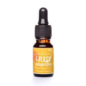 May include: A small amber glass bottle with a black dropper top. The label is yellow with orange and green accents and reads "CRISP Autumn Blend Fine Seasons Essential Oils".