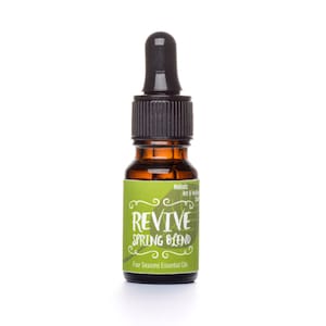 May include: A small brown glass bottle with a black dropper top. The bottle has a green label with the text "REVIVE SPRING BLEND" and "Four Seasons Essential Oil".