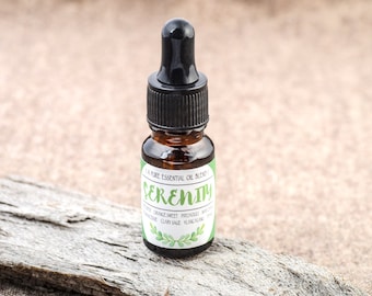 Puede incluir: Un pequeño frasco de vidrio marrón con un gotero negro. El frasco tiene una etiqueta blanca que dice "Serenity 100% Pure Essential Oil Blend" y enumera los ingredientes: Naranja dulce, Pachulí, Ylang Ylang, Salvia esclarea y Lima.