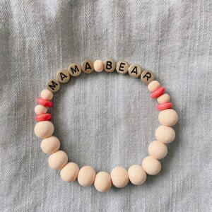 May include: A pink and white beaded bracelet with the words "MAMA BEAR" spelled out in silver letters.