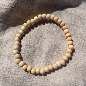 Op de afbeelding: Een eenvoudige houten kralen armband in een natuurlijke beige kleur. De armband is gemaakt van ronde kralen en is geregen op een dun koord.