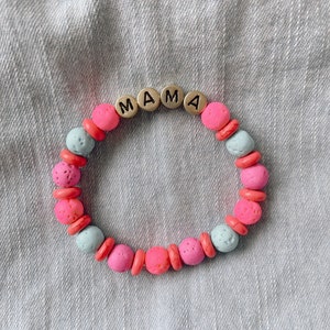 May include: A pink and blue beaded bracelet with the word "MAMA" spelled out in silver letters.