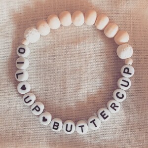 May include: A white wooden bead bracelet with the words "I love buttercup" spelled out in black letters.