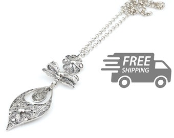 May include: A silver-toned filigree necklace featuring a delicate chain and a pendant composed of a bow, a flower, and a teardrop-shaped frame containing a small floral motif. The intricate metalwork displays fine, swirling wire patterns.
