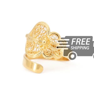 May include: A gold filigree ring with a delicate floral design. The ring is open and adjustable to fit different finger sizes.