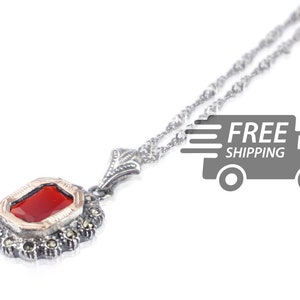 May include: A silver necklace with a red gemstone pendant set in a silver filigree design. The pendant is surrounded by small silver beads.
