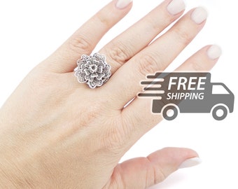 May include: A silver ring featuring a detailed filigree floral design. The metalwork consists of intricate, thin wire loops arranged in a layered, multi-petaled flower shape that sits prominently on the finger, showcasing a delicate, openwork texture.