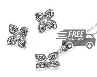 May include: A jewelry set consisting of two flower-shaped stud earrings and a matching pendant on a silver chain. Each piece features a four-petaled design with dark blue enamel accents and intricate silver filigree detailing throughout the petals.