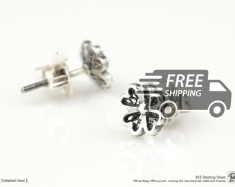 May include: A pair of sterling silver stud earrings shaped like four-leaf clovers. Each earring features a polished silver outline with a dark, recessed center and a small silver bead in the middle. The earrings include standard silver post backs.
