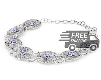 Puede incluir: Una pulsera de plata con una serie de eslabones circulares de filigrana, cada uno centrado con una pequeña flor de esmalte azul. La pulsera incluye una delicada cadena de extensión con un cierre de mosquetón y metal detallado.