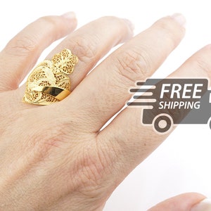 May include: A gold filigree ring with a delicate, intricate design. The ring is worn on a finger and is a statement piece of jewellery.