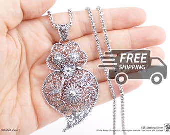 Op de afbeelding: Een zilveren hangerketting met een ingewikkeld filigraan hartontwerp met bloemaccenten. De hanger hangt aan een getextureerde zilveren ketting. Het metaal is gemarkeerd als 925 sterling zilver, wat de samenstelling aangeeft.