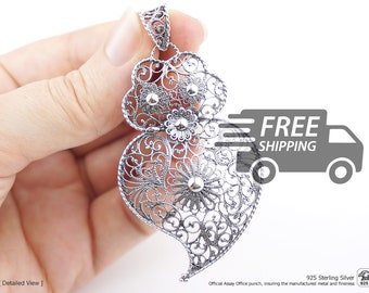 Op de afbeelding: Een zilveren filigraan hanger in de vorm van een hart met ingewikkelde draadpatronen en kleine bolvormige accenten. Het sieraad heeft een oogje aan de bovenkant en bevat onderaan de tekst 925 Sterling Silver.