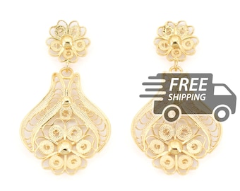 May include: A pair of gold-tone drop earrings featuring intricate filigree metalwork. Each earring consists of a small flower-shaped stud connected to a larger, bell-shaped pendant with a central floral motif and delicate swirling wire patterns.