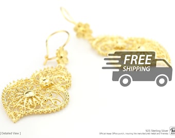May include: A pair of gold-toned drop earrings featuring intricate filigree heart-shaped pendants. Each earring is suspended from a small flower-shaped stud with a hook closure. The metalwork displays a delicate, open-work pattern.
