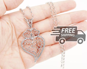 Op de afbeelding: Een zilverkleurige filigraan hart-hanger ketting met een ingewikkeld, opengewerkt metalen ontwerp met kleine bolvormige accenten. De hanger hangt aan een bijpassende zilverkleurige schakelketting en toont een gedetailleerd, kantachtig patroon.