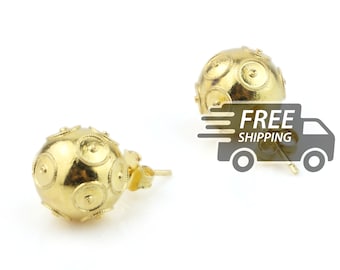 May include: A pair of gold stud earrings featuring a spherical design. Each earring is decorated with multiple raised circular motifs that have a textured, beaded border and a small central point. The earrings include standard post backings.
