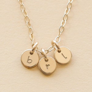 May include: A gold chain necklace with three small round charms, each with a letter engraved on it. The letters are "b", "r", and "l".