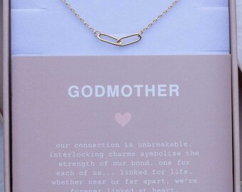 May include: A pink gift box containing a gold necklace with two interlocking charms. The box features the text "GODMOTHER" and "our connection is unbreakable. interlocking charms symbolize the strength of our bond. one for each of us... linked for life. whether near or far apart, we're forever linked at heart. everly made".
