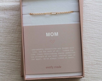 May include: A gold chain bracelet with a small, rectangular charm in a pink box. The box has a card with the word "MOM" and a message about unbreakable connections.