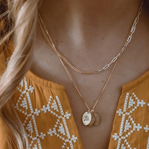 May include: A gold chain necklace with a delicate silver chain layered on top. The gold chain has three small, round pendants with a floral design.