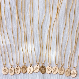 May include: A set of 14 gold necklaces with delicate chains and oval pendants featuring different floral designs. Each pendant has a unique embossed flower motif.