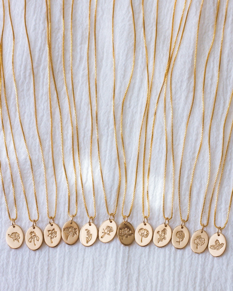 May include: A set of 14 gold necklaces with delicate chains and oval pendants featuring different floral designs. Each pendant has a unique embossed flower motif.
