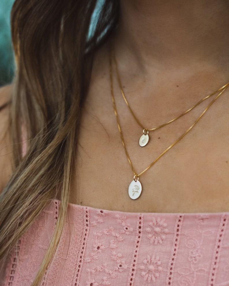 May include: Two gold chain necklaces with oval pendants. The top pendant is plain, while the bottom pendant features a delicate floral design.