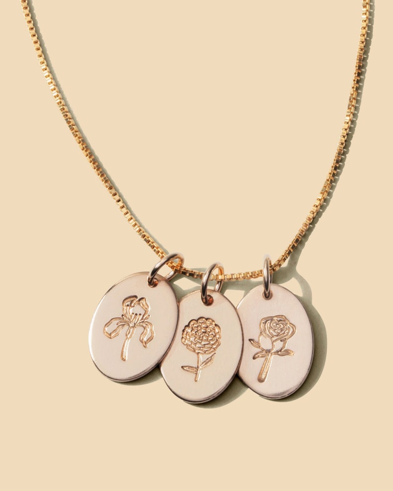 May include: A gold chain necklace with three oval-shaped pendants. Each pendant features a different flower design: an iris, a carnation, and a rose.