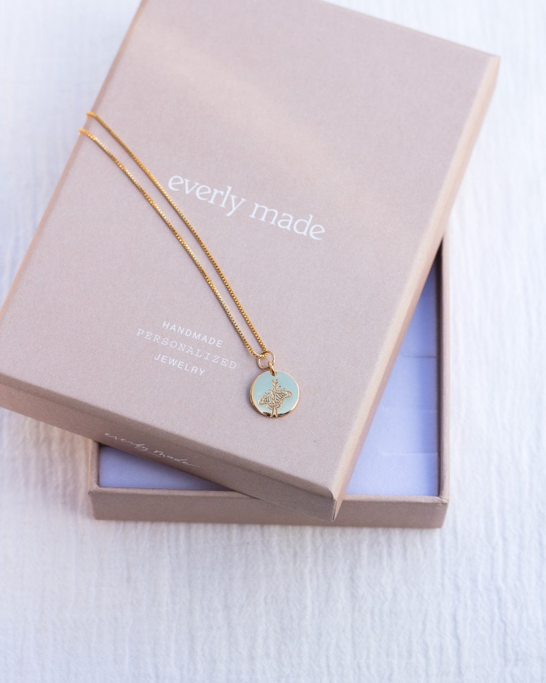 May include: A gold chain necklace with a delicate pendant featuring a floral design. The necklace is in a light brown box with the text "everly made" and "handmade personalized jewelry" printed on it.