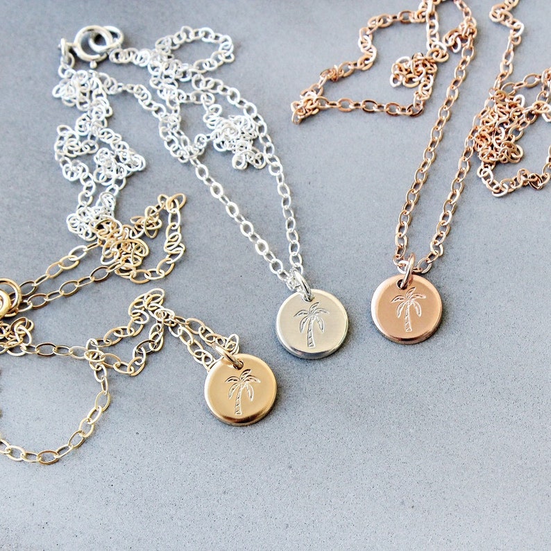 Pu&ograve; includere: Tre delicate collane con ciondoli a forma di palma. Le collane sono in argento, oro e oro rosa.
