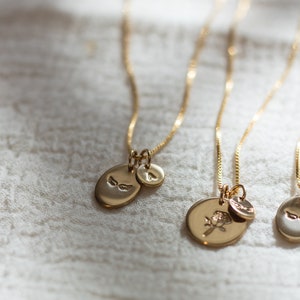 May include: Three gold necklaces with different charms. The first necklace has a small oval charm with a pair of wings, the second necklace has a larger oval charm with a rose design, and the third necklace has a small oval charm with a pair of wings.