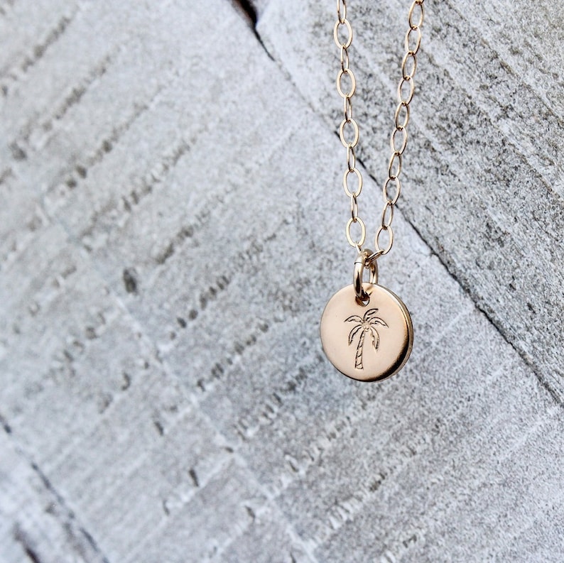 Pu&ograve; includere: Una collana d'oro con un piccolo ciondolo rotondo con un design a forma di palma.