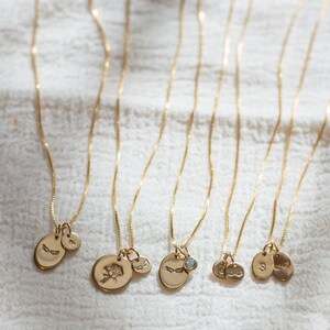 May include: Six gold necklaces with different charms, including a rose, a small diamond, and initial letters. The necklaces are on a white fabric background.