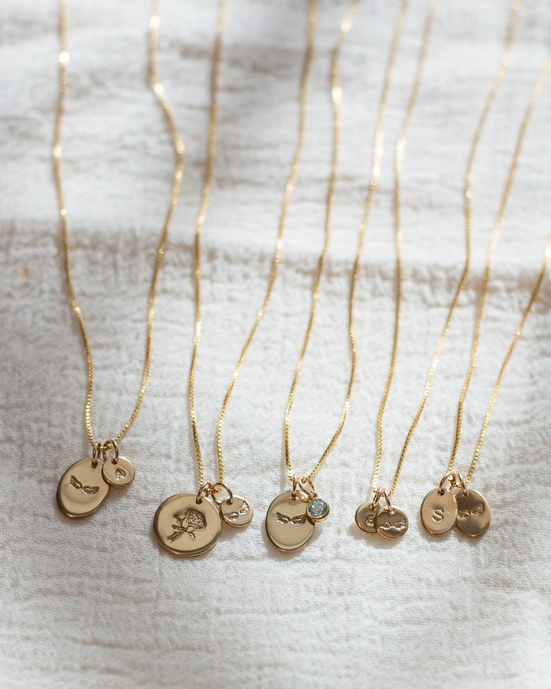May include: Six gold necklaces with different charms, including a rose, a small diamond, and initial letters. The necklaces are on a white fabric background.