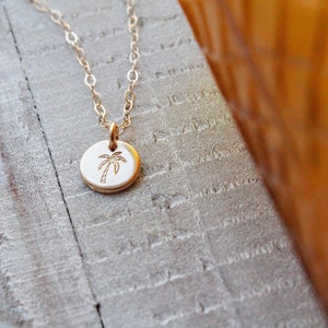 Pu&ograve; includere: Una collana d'oro con un piccolo ciondolo rotondo che presenta un design a forma di palma. Il ciondolo &egrave; su una catena delicata.