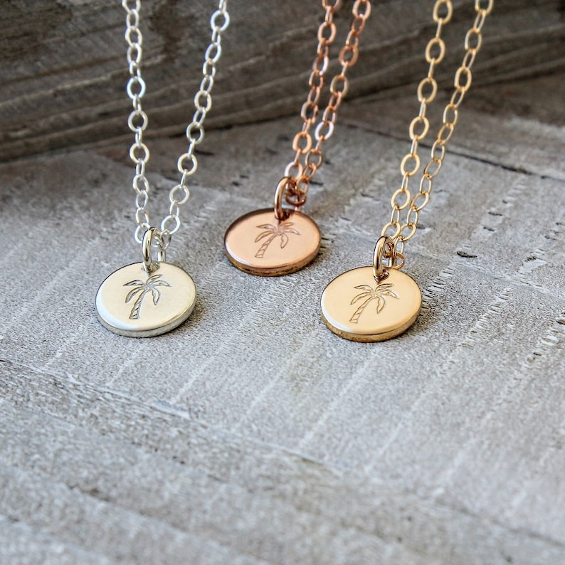 Pu&ograve; includere: Tre delicate collane con ciondoli a forma di palma. Le collane sono in argento, oro e oro rosa. Le palme sono incise su piccoli dischi rotondi.