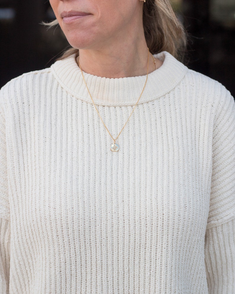 May include: A white cable knit sweater with a gold chain necklace and a small round pendant.