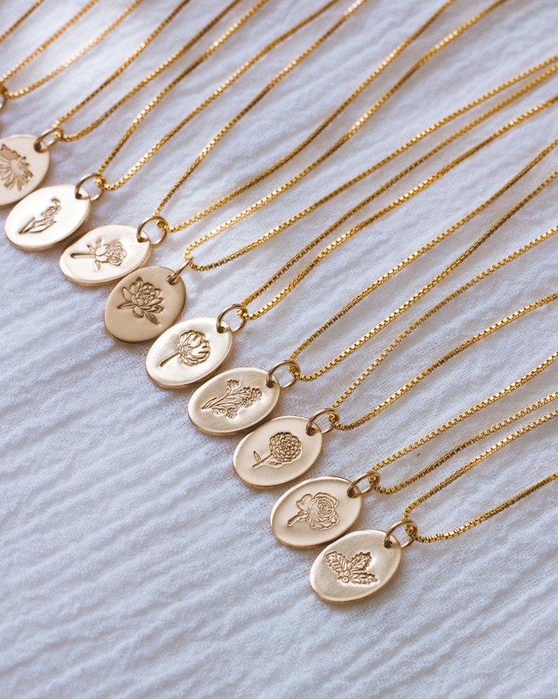 May include: A set of gold chain necklaces with oval pendants featuring different floral designs. Each pendant has a delicate, embossed floral motif.