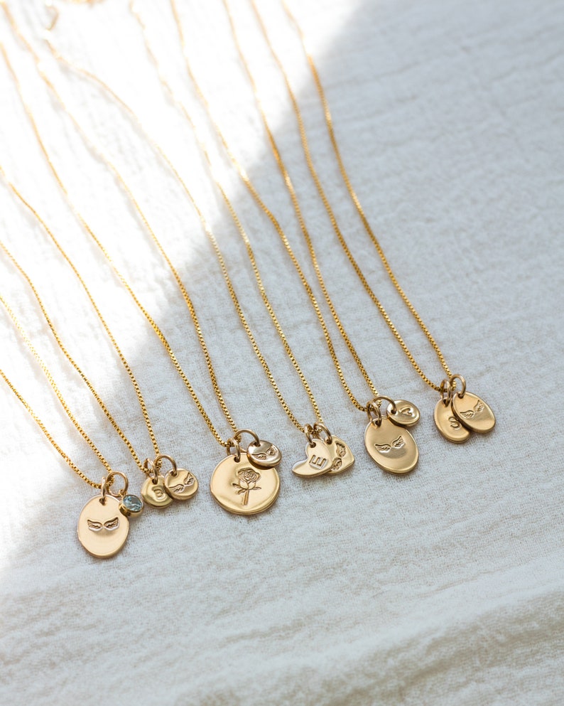 May include: A set of nine gold necklaces with different charms, including a heart, a flower, and wings. The necklaces are on a white fabric background.