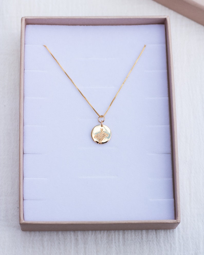 May include: A gold chain necklace with a round pendant featuring a delicate engraved design. The necklace is displayed in a white velvet-lined box.