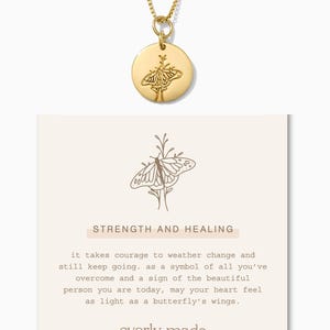May include: Gold necklace with a round pendant featuring a butterfly design. The pendant is engraved with the words "Strength and Healing". The card below the necklace reads "it takes courage to weather change and still keep going. as a symbol of all you've overcome and a sign of the beautiful person you are today, may your heart feel as light as a butterfly's wings. everly made"