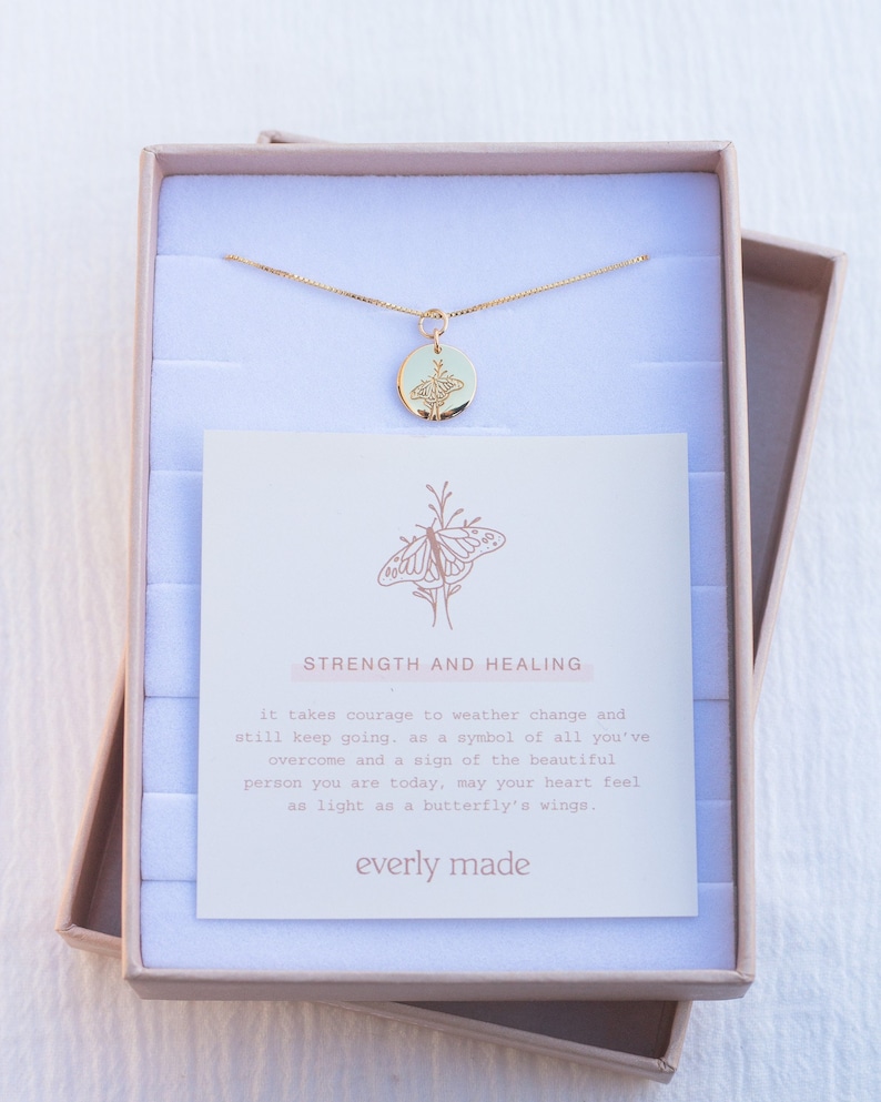 May include: A gold necklace with a round pendant featuring a butterfly design. The necklace comes in a small box with a card that reads "Strength and Healing" and includes a message about overcoming challenges and feeling light as a butterfly's wings. The card is signed "everly made".