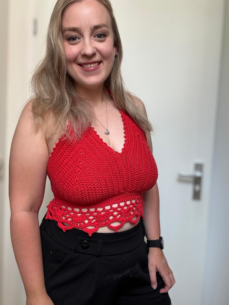 May include: A red halter top with a crocheted design. The top features a scalloped edge at the waist and a halter neck. The top is paired with black pants. The top is handmade.