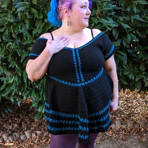 May include: Black crochet top with off-the-shoulder sleeves and a flared skirt. The top is accented with blue stitching along the neckline, sleeves, and skirt hem. The model is wearing purple leggings.