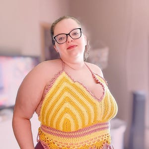 May include: A handmade crochet halter top in yellow and pink. The top features a chevron pattern in yellow and is trimmed with pink crochet. The bottom edge of the top has a scalloped design. The top is worn with burgundy leggings.