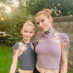 May include: Two people wearing crocheted tops. The top on the left is gray with a spiderweb design and the top on the right is purple with a floral design.