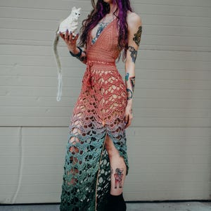Peut inclure: Robe en crochet faite &agrave; la main dans un d&eacute;grad&eacute; de couleurs, passant du p&ecirc;che au turquoise et se terminant par du vert fonc&eacute;. La conception ajour&eacute;e pr&eacute;sente un d&eacute;collet&eacute; licou et une fente haute sur la cuisse. La robe est associ&eacute;e &agrave; des bottines &agrave; plateforme noires.