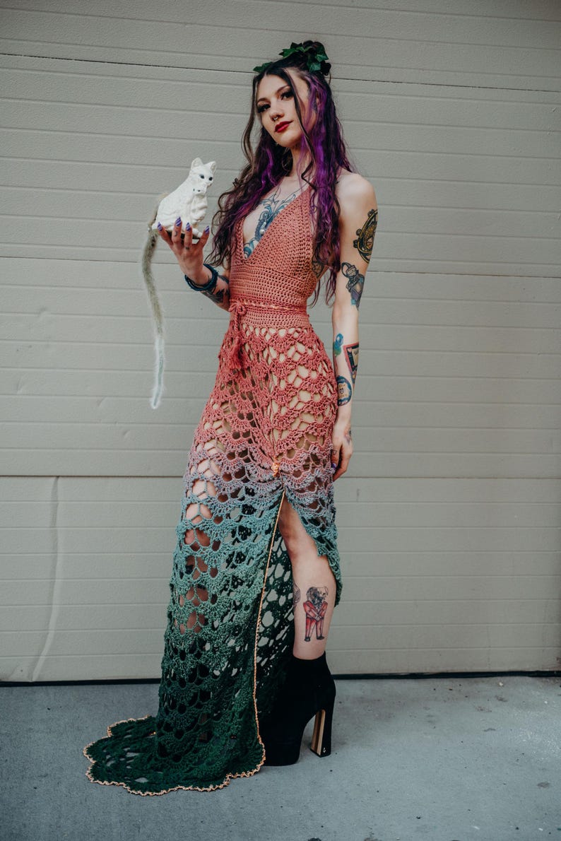 Peut inclure: Robe en crochet faite &agrave; la main dans un d&eacute;grad&eacute; de couleurs, passant du p&ecirc;che au turquoise et se terminant par du vert fonc&eacute;. La conception ajour&eacute;e pr&eacute;sente un d&eacute;collet&eacute; licou et une fente haute sur la cuisse. La robe est associ&eacute;e &agrave; des bottines &agrave; plateforme noires.