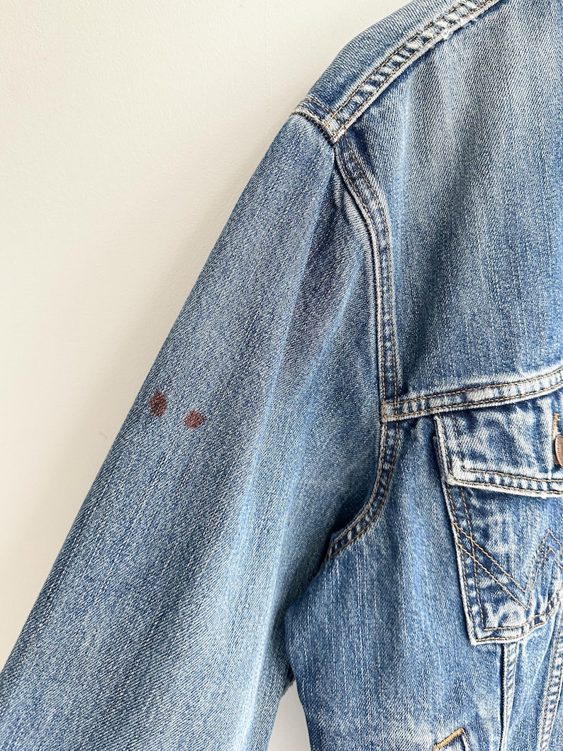 May include: A blue denim jacket with a brown stain on the left sleeve.